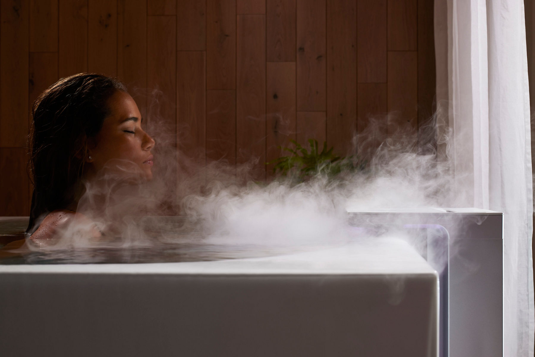 Image of a woman soaking in a luxurious Kohler bathtub with steam rising from the water. She has her eyes closed and is immersed in the steam and relaxation of the bath experience. 
