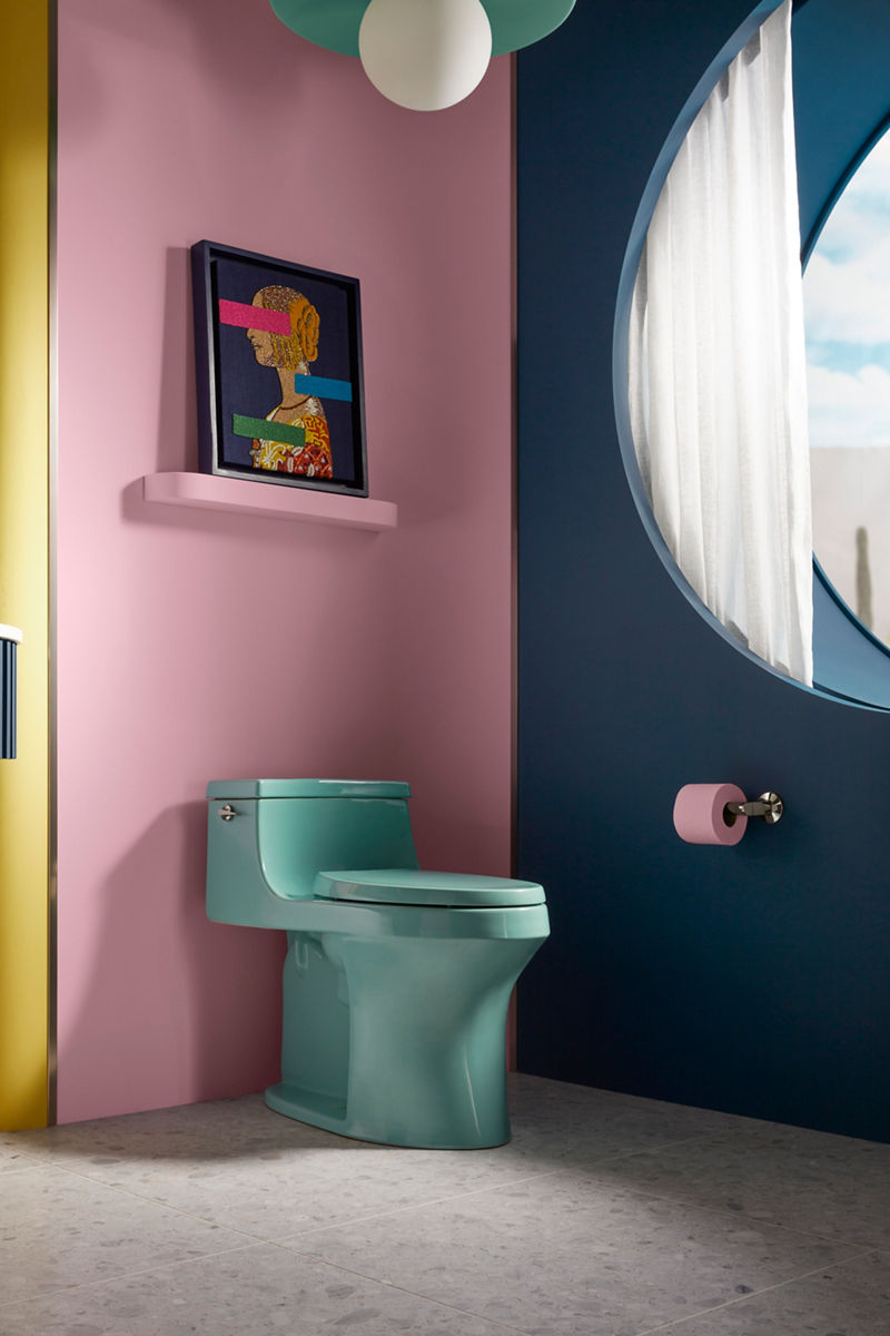 Image of the toileting space in the bathroom designed by Jonathan Adler, featuring the Spring Green San Souci one-piece toilet against a pink wall, showing the Vibrant Polished Nickel trip lever handle and matching toilet paper holder. 