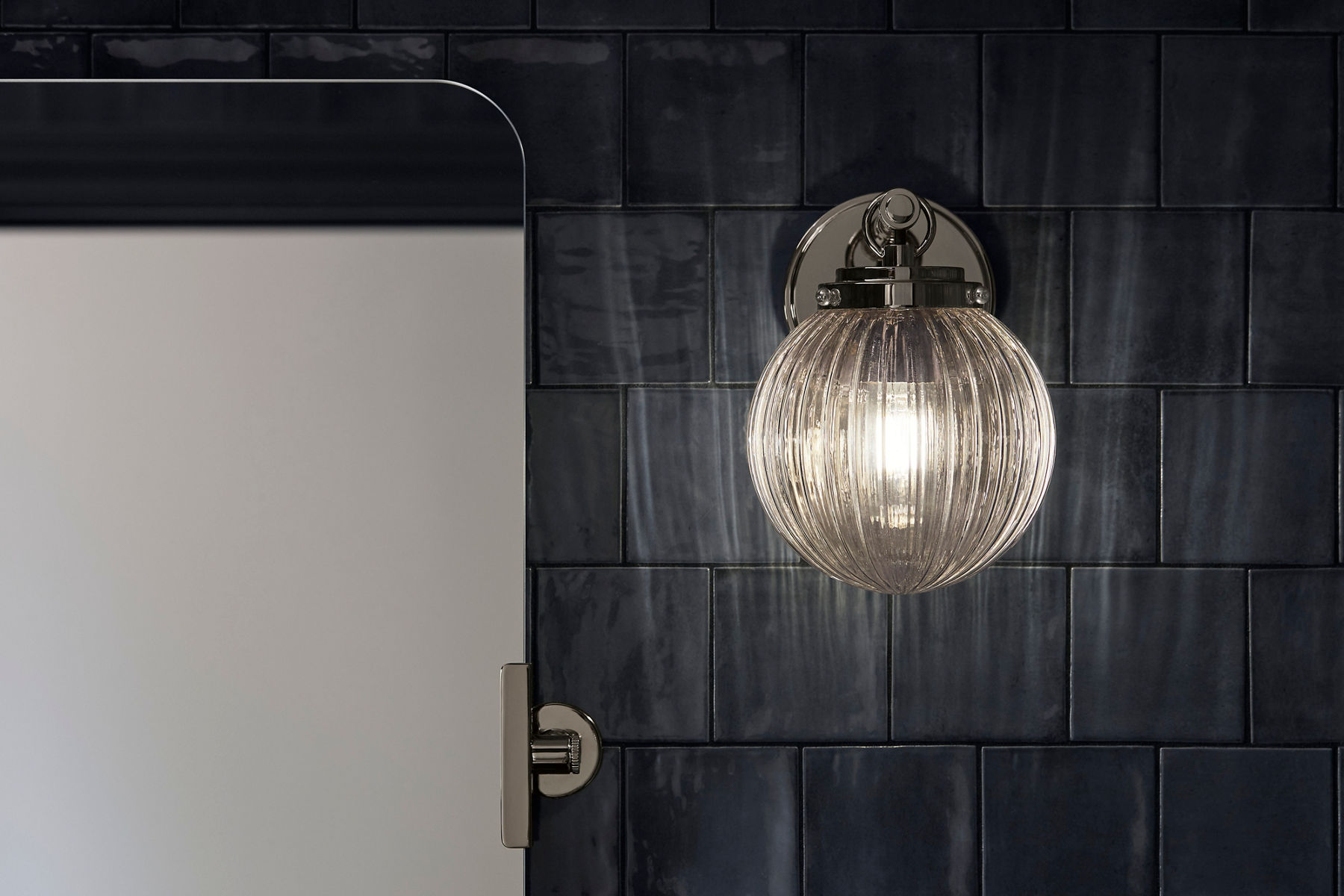 Une applique en verre et en chrome sur un mur en carrelage bleu foncé.