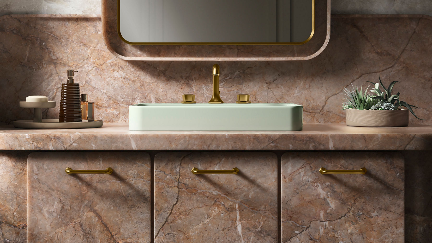Image en gros plan d’un meuble-lavabo en marbre brun rose avec trois armoires et des poignées d’armoires dorées. Un lavabo vert pâle avec un robinet doré est fixé au comptoir de la salle de bain. Un miroir rectangulaire arrondi est suspendu au-dessus du lavabo, et un savon et des objets décoratifs sont soigneusement disposés sur le comptoir de la salle de bain.