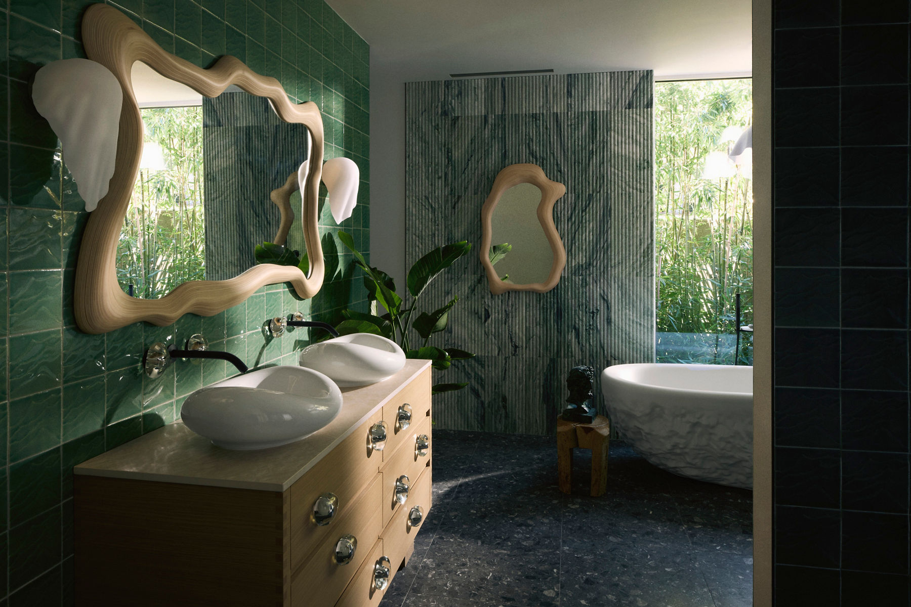 Modern bathroom interior featuring a double vanity with sculptural sinks, wavy mirrors, green tiled walls, and artistic decor. A freestanding bathtub with textured exterior is visible near a large window, surrounded by greenery and natural light.