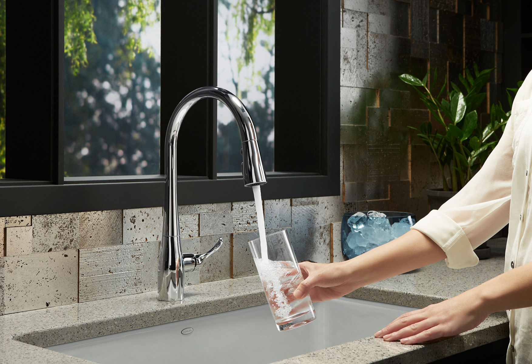 A hand holding a glass under a kitchen faucet with water filling it.