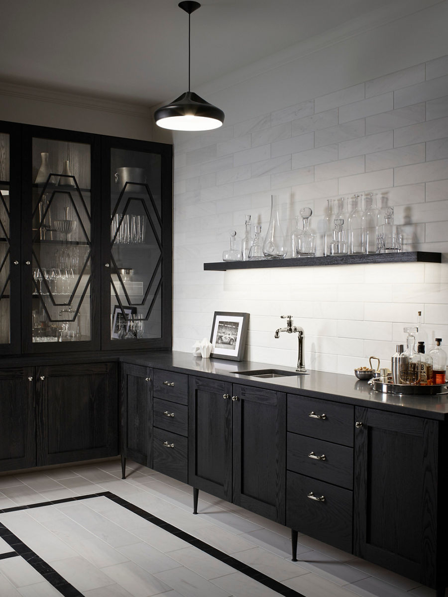 A KOHLER Artifacts Gentleman's bar sink installed on  a black countertop, underneath a shelf of clear glass bottles.