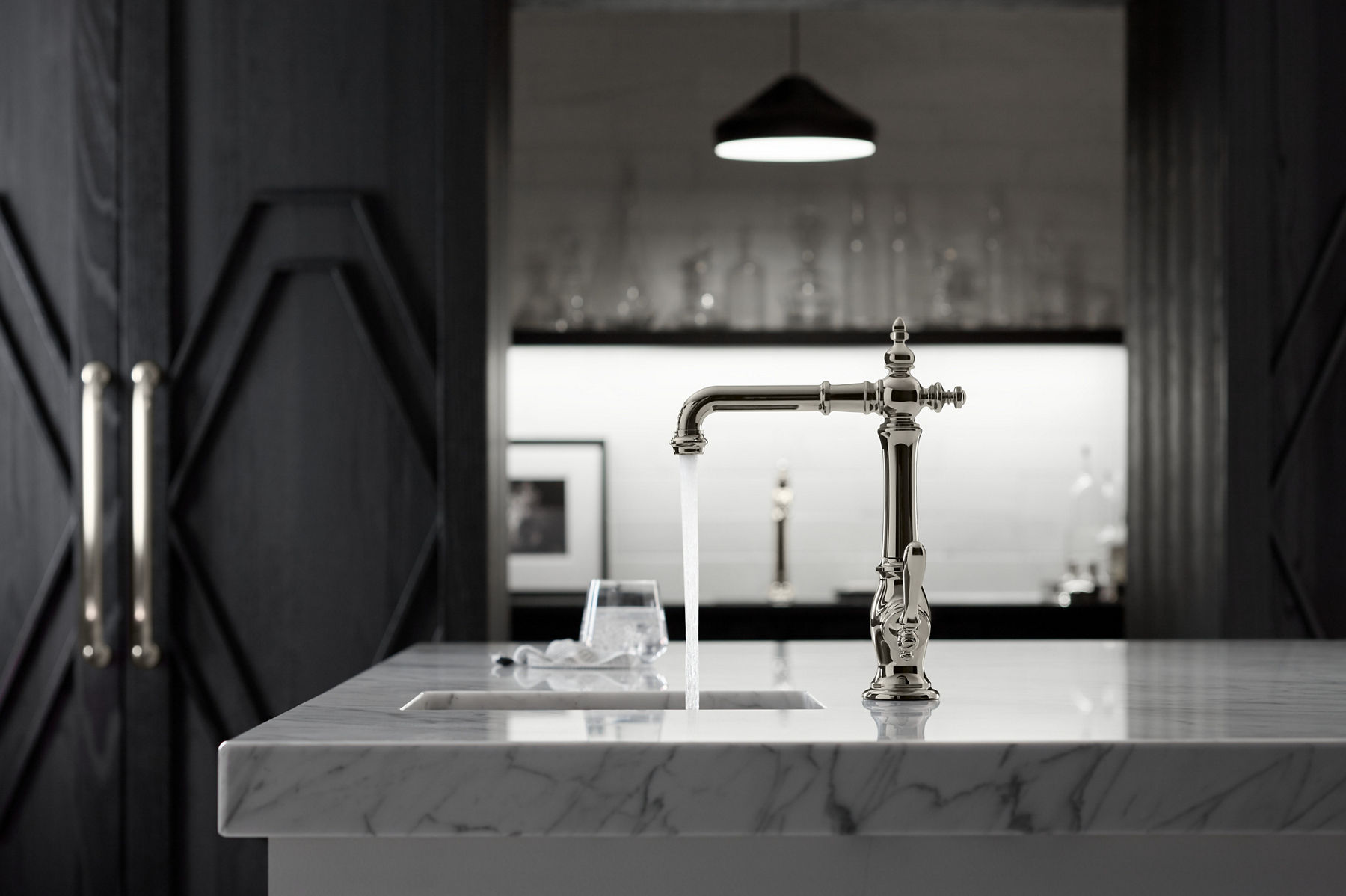 Water flows from a KOHLER Artifacts bar sink faucet with Victorian spout design installed on a white marble island.