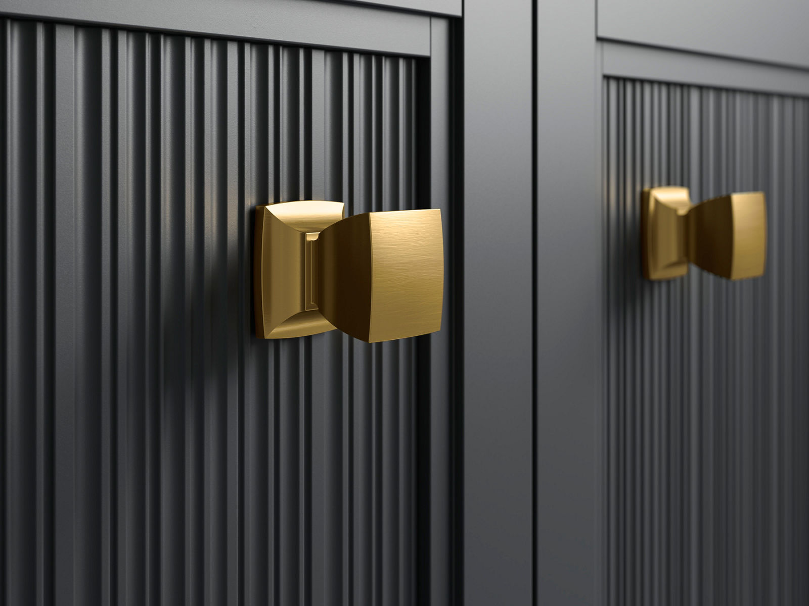 Close-up image of two cabinet door pull knobs in vibrant brass finish, against a black textured wood cabinet door. 