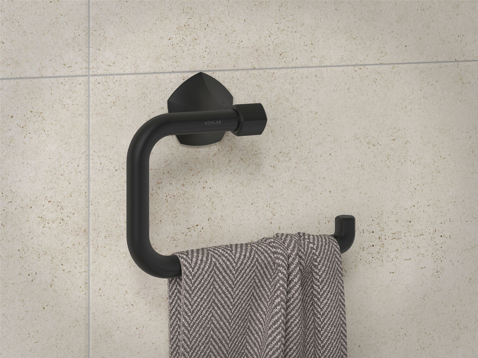 Close-up image of a matte black Kohler bathroom hand towel hanger, installed on a neutral tiled wall.