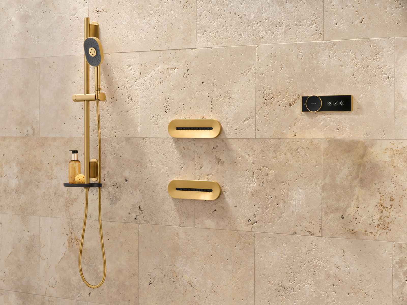 Image of a shower with natural cream-colored stone tile and Kohler Statement and Anthem shower heads and shower controls in a vibrant brass finish. The hand shower is installed next to two body sprays and the control panel to the side.