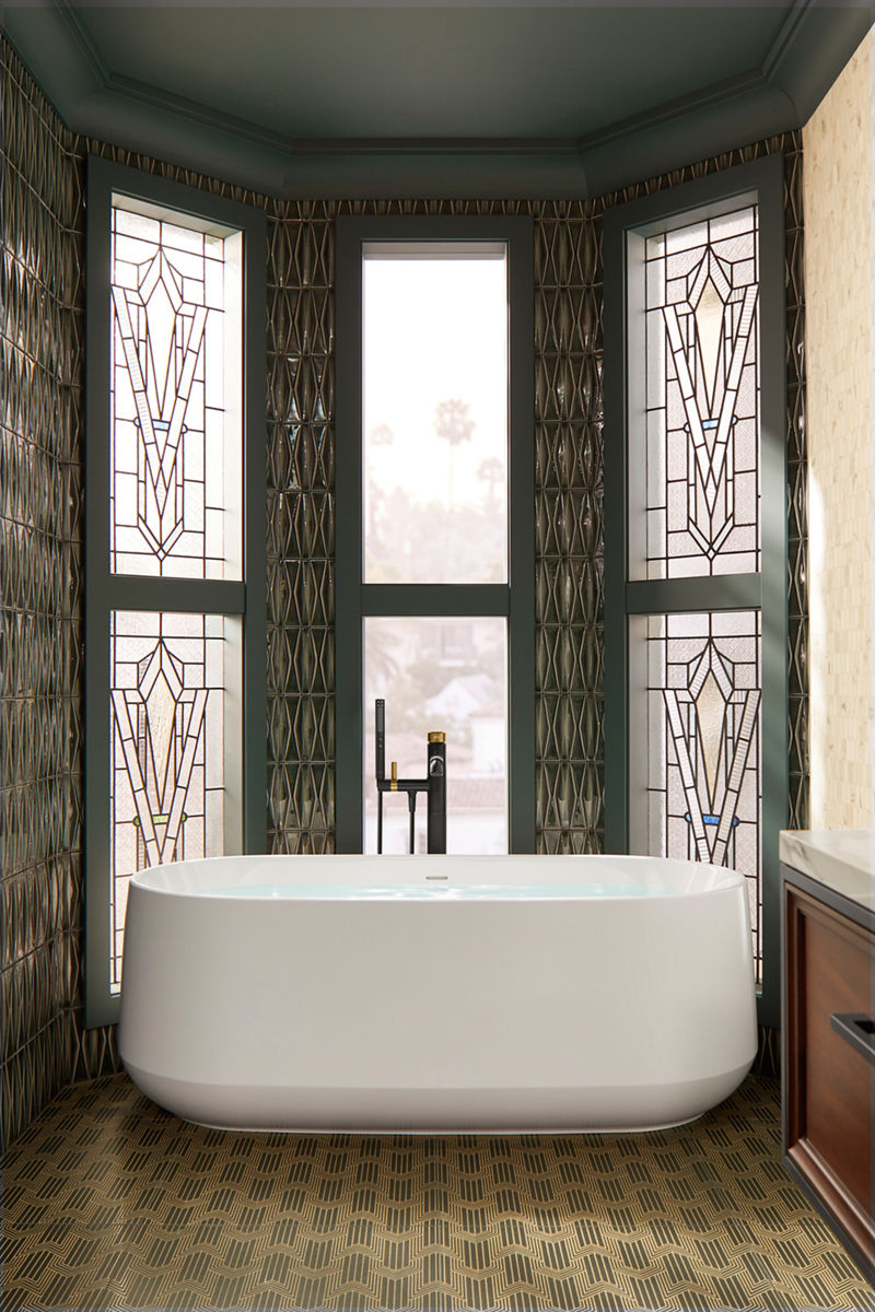 A white freestanding bath with two-tone black and brass bath filler surrounded by leaded-glass windows with grayish-green trim.