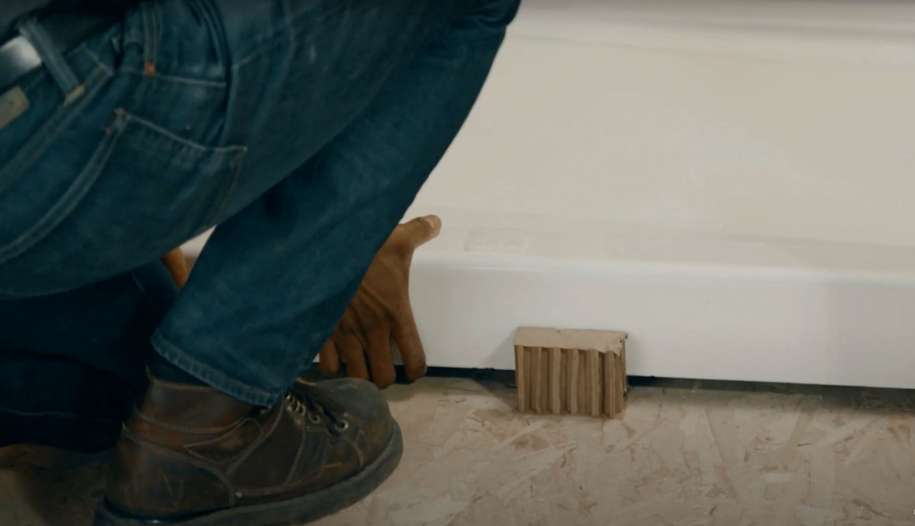 Detail of a cast iron shower base being lowered onto a bathroom subfloor.