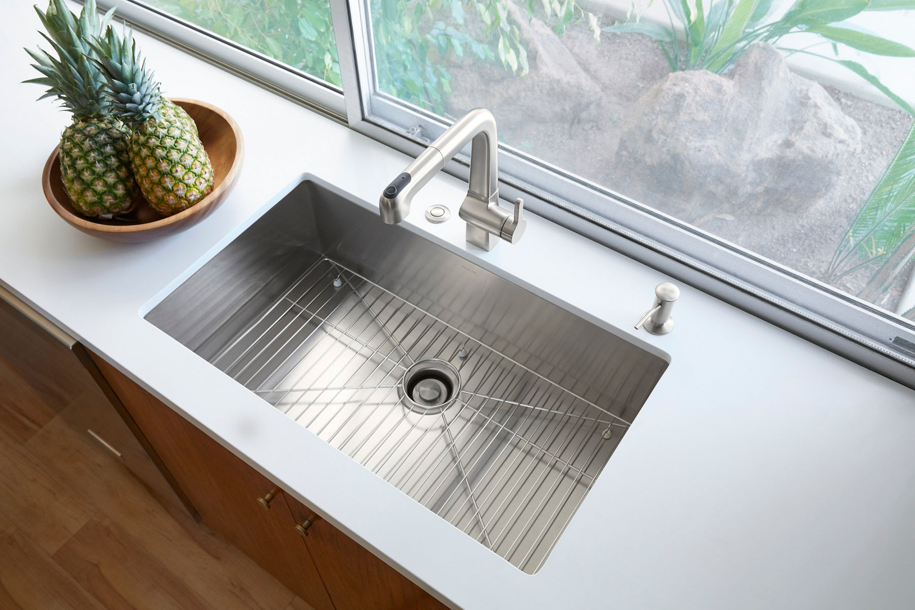 An undermount stainless steel kitchen sink with sharp 90-degree angles on the sides and bottom with a stainless steel faucet and light gray countertop.