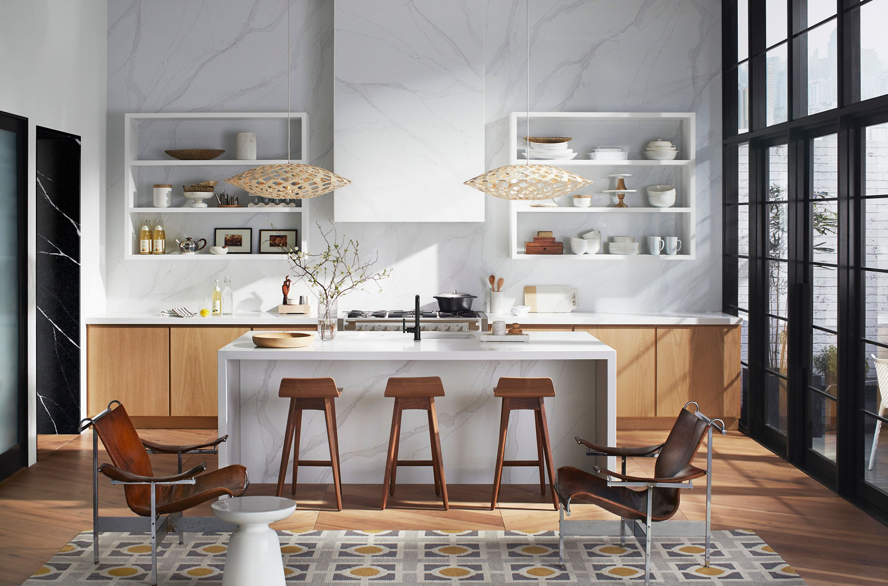 A bright kitchen with a white island and wooden bar stools, open shelving with dishes, and decorative pendant lights featuring light wood cabinetry and a sleek stove.