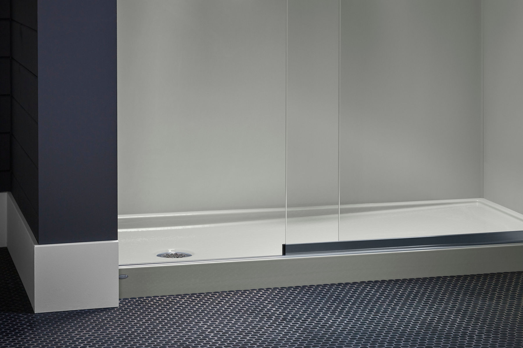 A view of the lower portion of a shower area, showing the shower base, sliding glass door, and small-tiled floor and wall in a dark blue color.