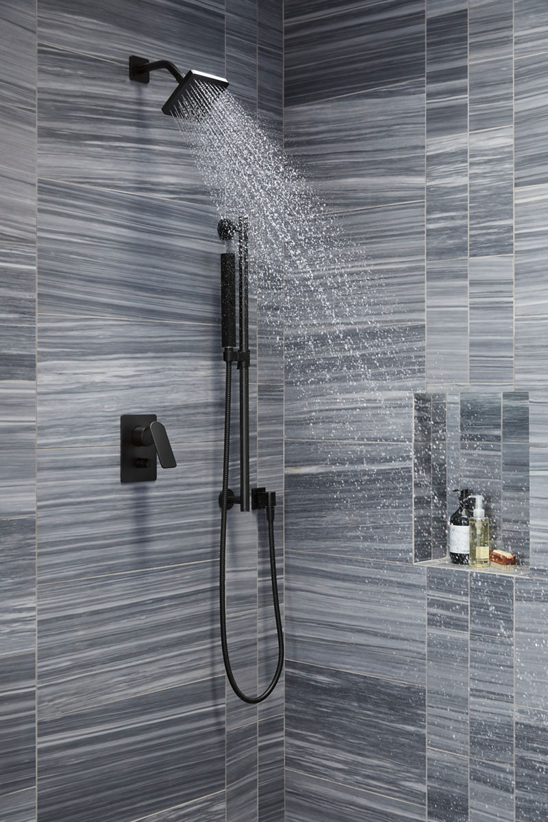 Close up of a matte black square showerhead with water coming out of it in a square pattern, installed on a multi-toned gray tile wall with horizontal striping.