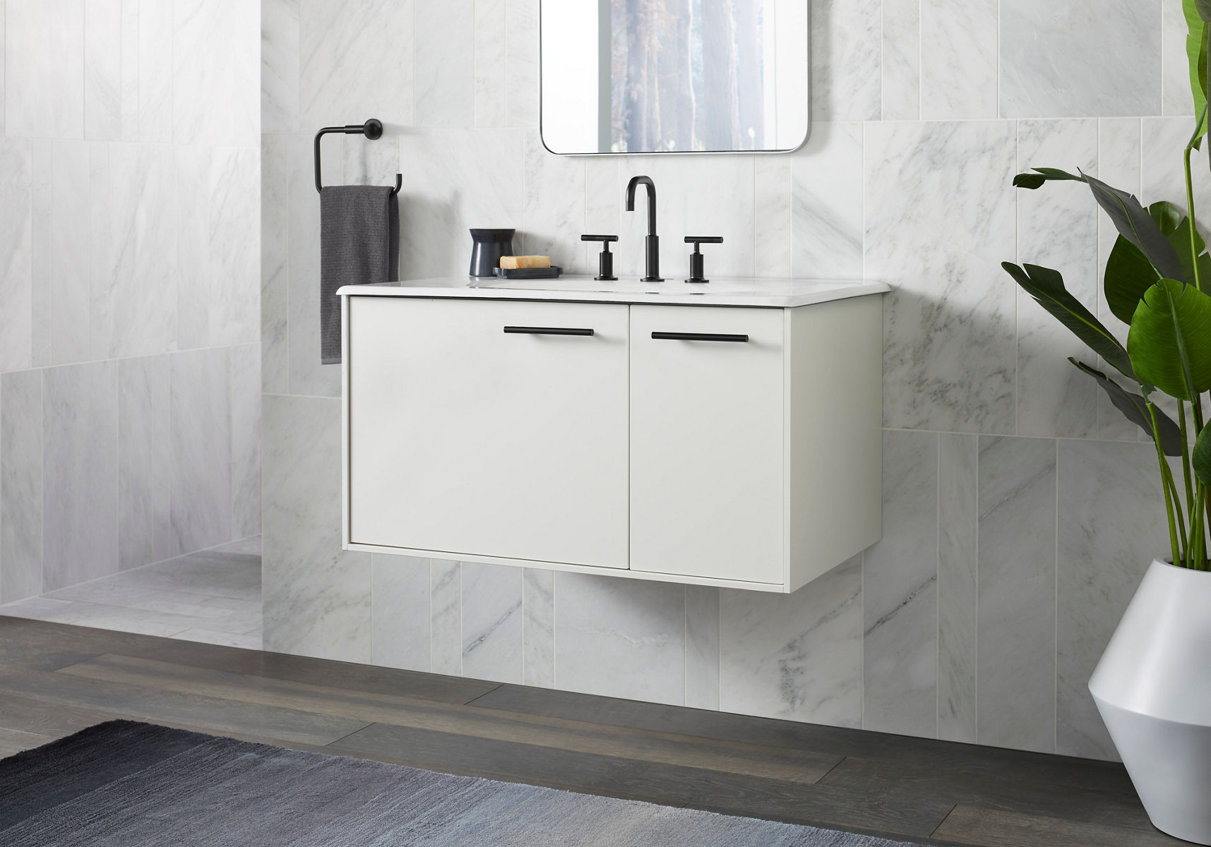 A white bathroom vanity with black hardware and a black widespread faucet against a white a wall with a mirror on it.