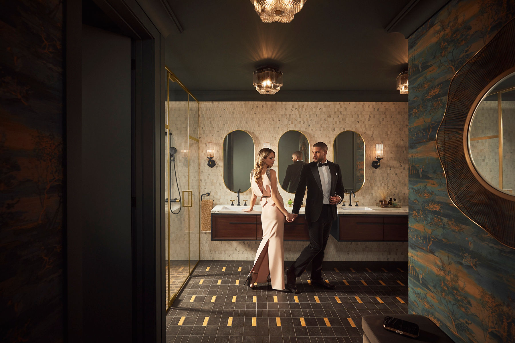 Image illustrant le design de salle de bain Classic Glam avec une grande douche et un meuble-lavabo double et des miroirs dans des finis noirs et dorés classiques, avec un couple glamour vêtu de tenues de soirée formelles debout dans la salle de bain.