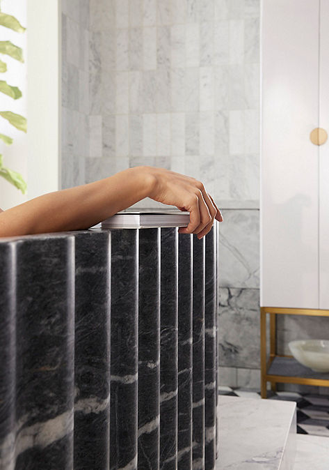 Detail shot of person sitting in black marble bathtub.