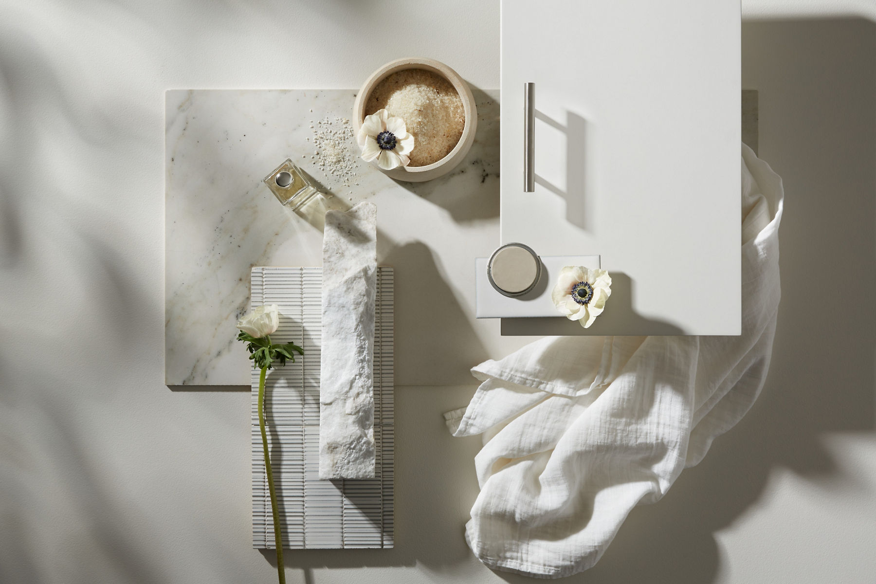 A designer's mood board with cabinet doors, handles, tile contrasting tile samples, and fabrics in shades of white, cream, and beige.