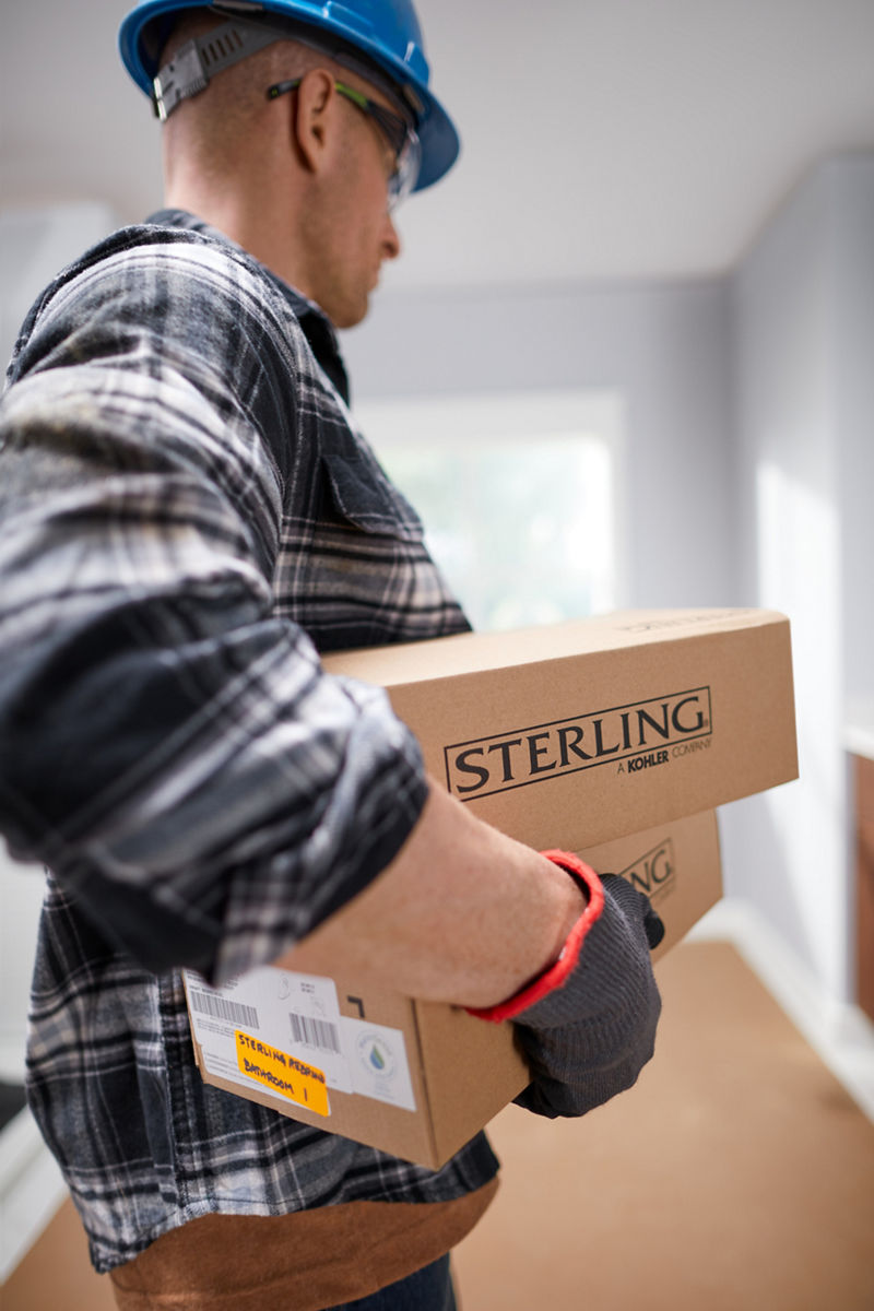 A man in a plaid shirt and hardhat carrying boxes with the Sterling logo.