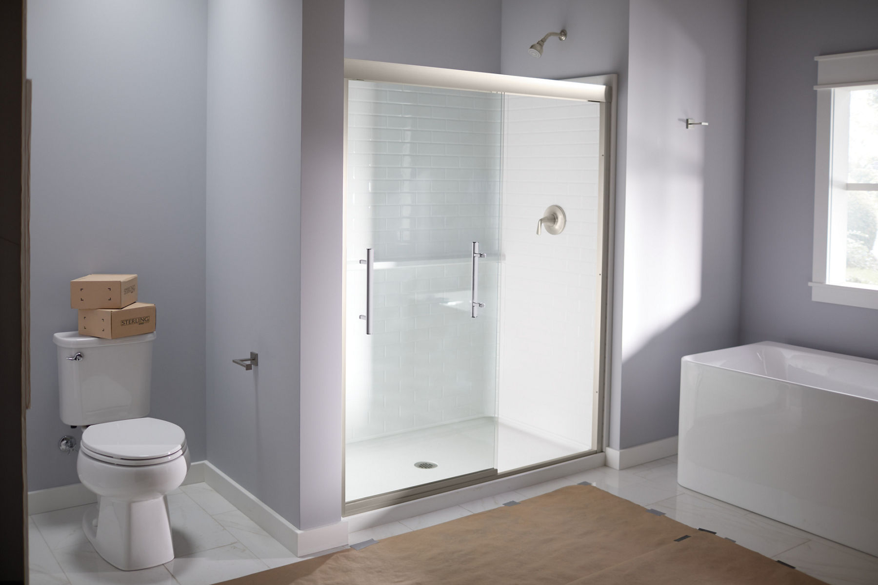 A clear sliding shower door with white shower base and surround installed in room with lavender walls.