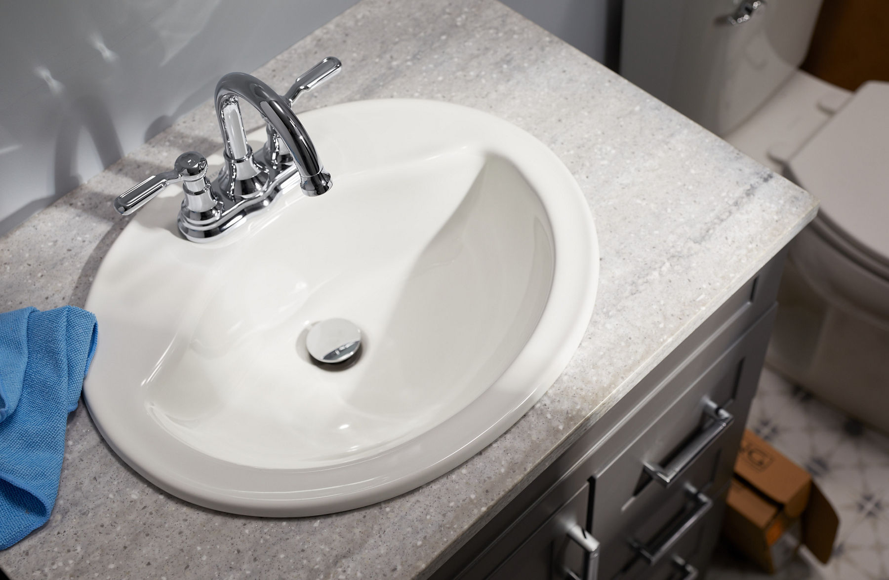 Overhead view of a white enameled cast iron sink with a chrome centerset faucet, on a gray stone counter top.