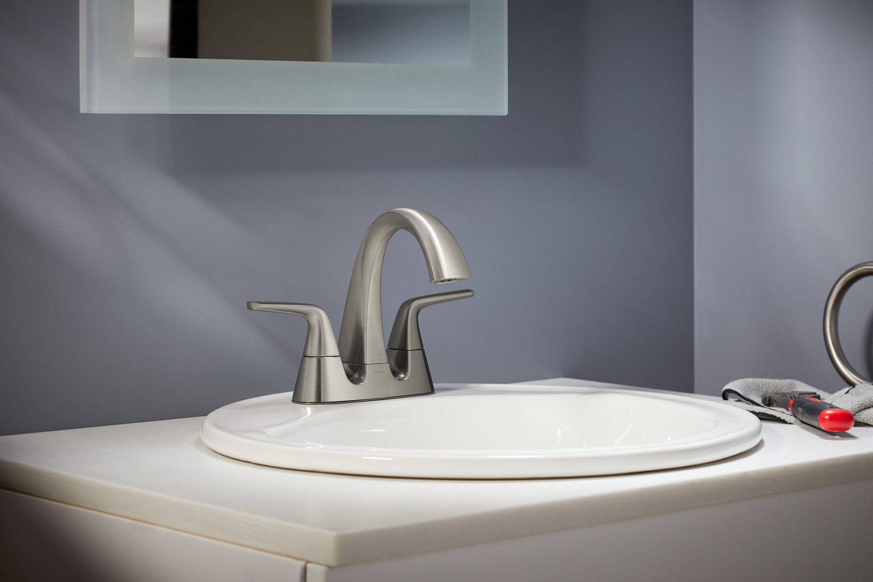 Centerset sink with long, graceful handles and spout in brushed nickel, on a white sink with gray walls in background.