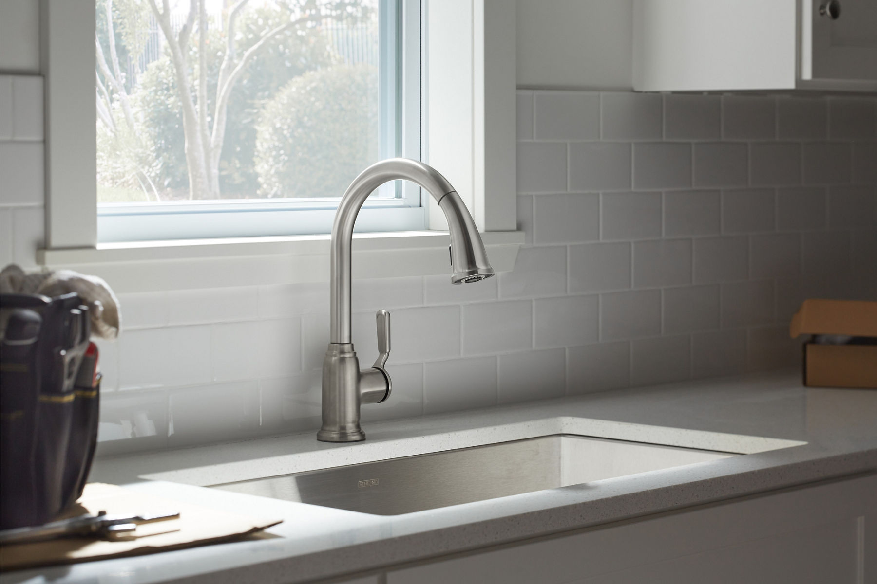 Stainless steel pull-down kitchen faucet on a white counter top with white walls behind it.