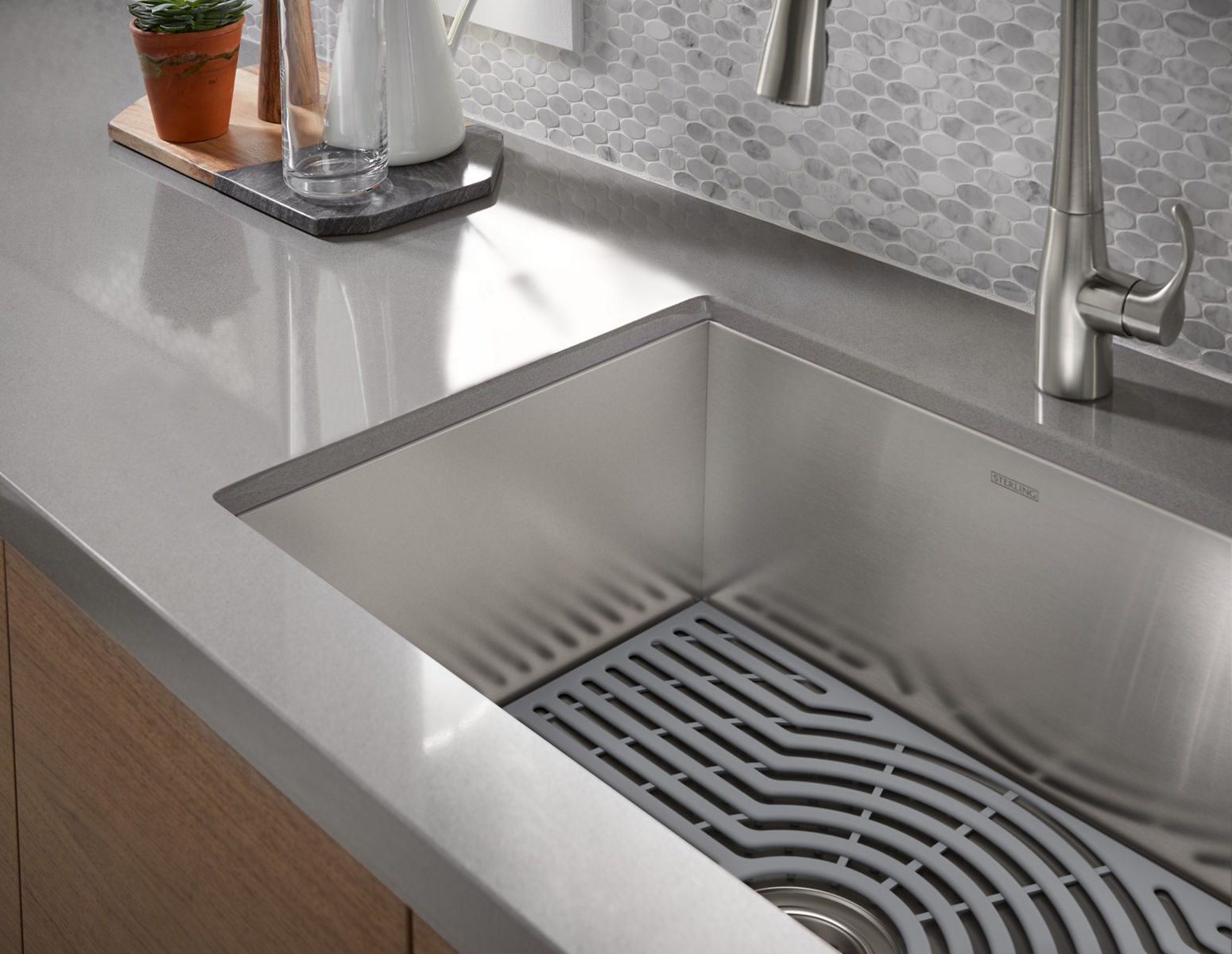 A stainless steel kitchen sink with a bottom tray, in a gray counter top and stainless steel faucet.