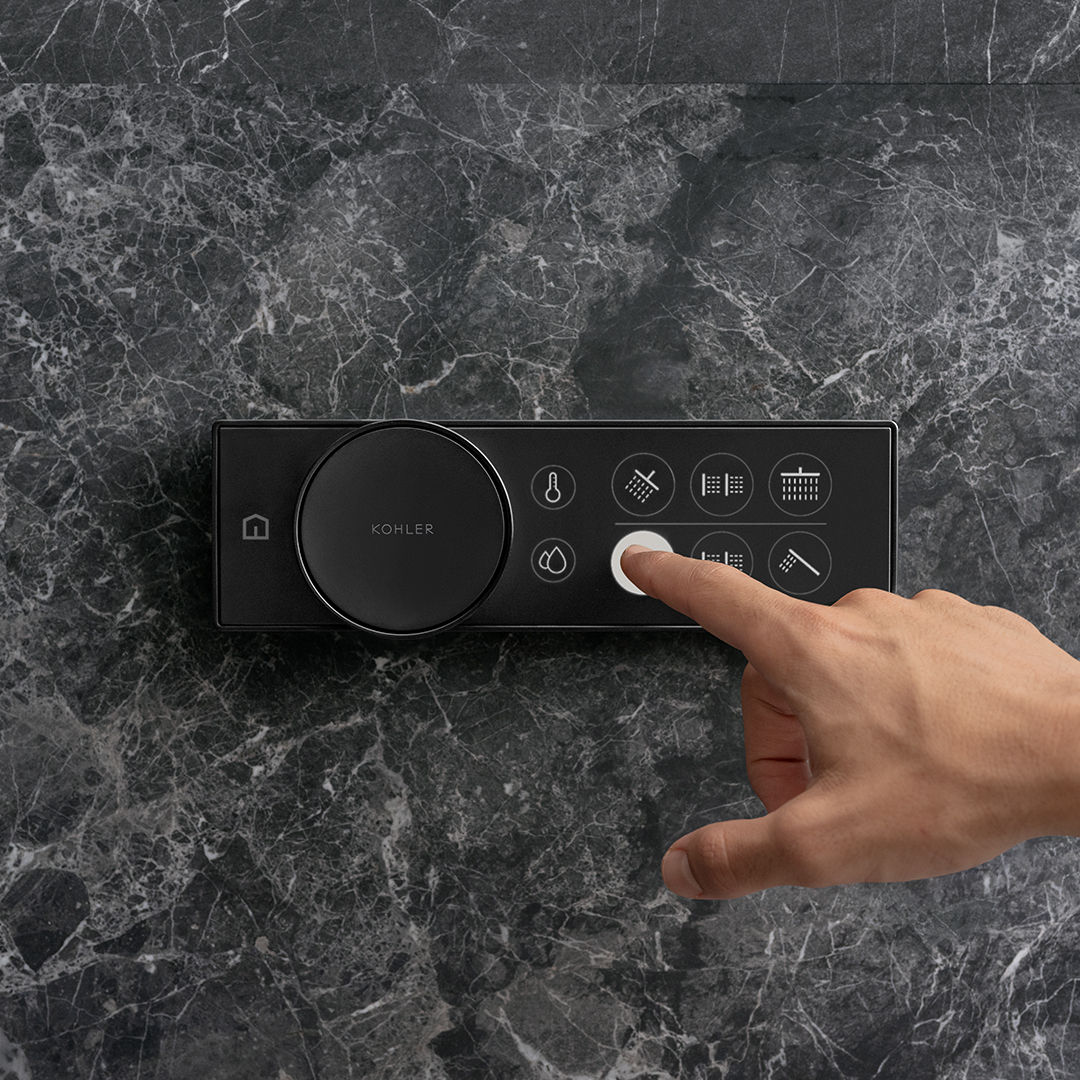 A person turns on their shower using a KOHLER Anthem digital shower control mounted on a black marble wall.