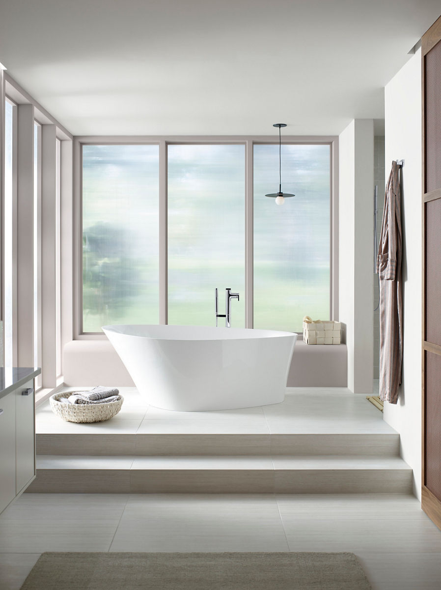 A Veil freestanding bath set in a large room on a raised floor in a room with a neutral color scheme with a large semi-opaque window looking out over a blurred nature scene.