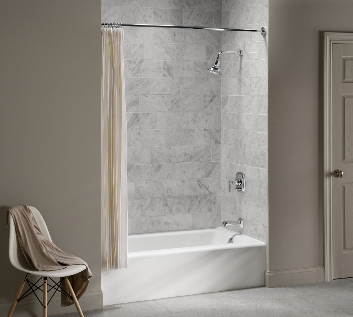 A white Bellwether bathtub with light gray veined tile walls, multiple grab bars and polished chrome bath and shower faucet components.