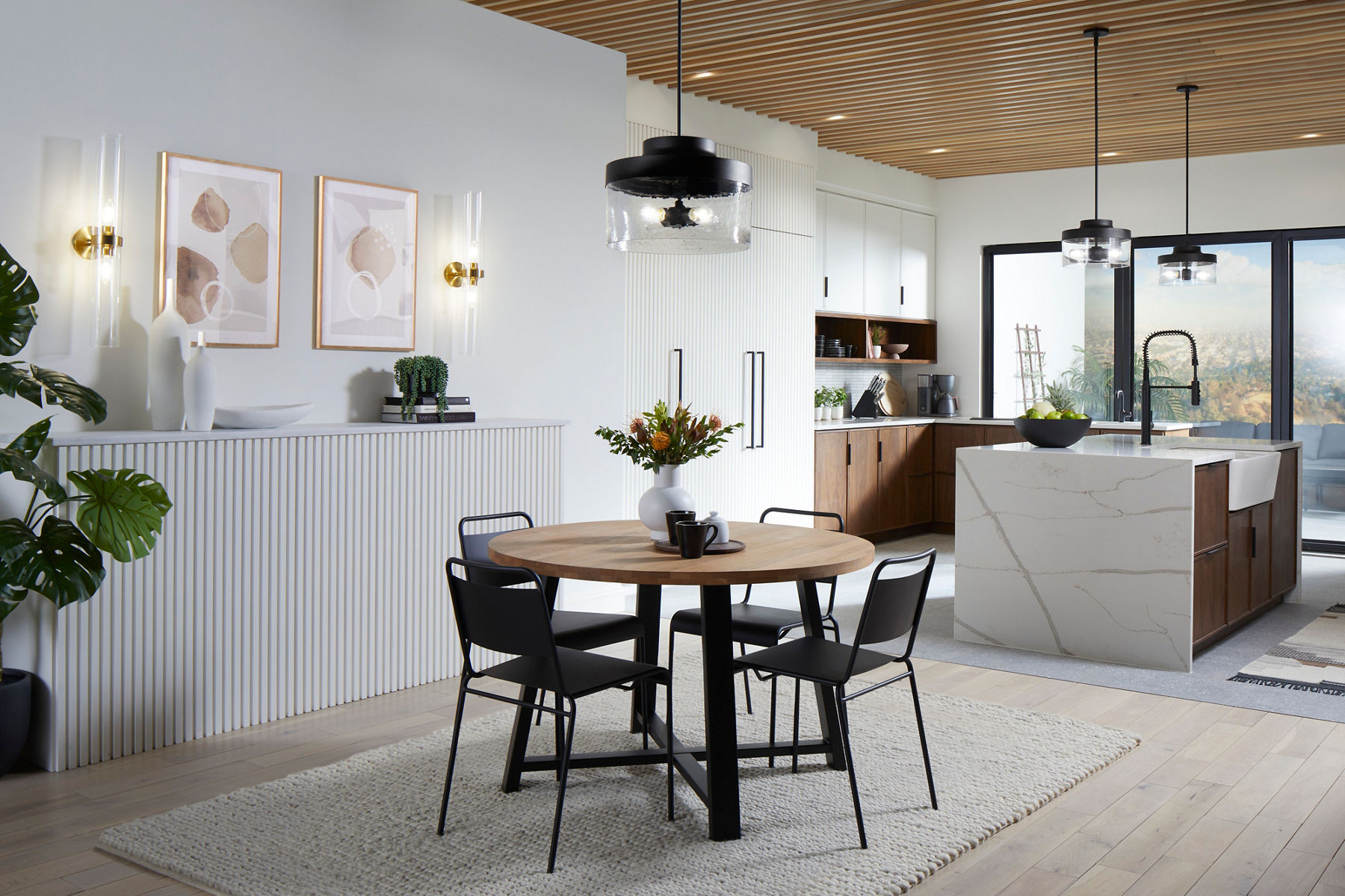 An open concept kitchen and dining space in tones of white, black and medium wood, with a large waterfall island in the kitchen.