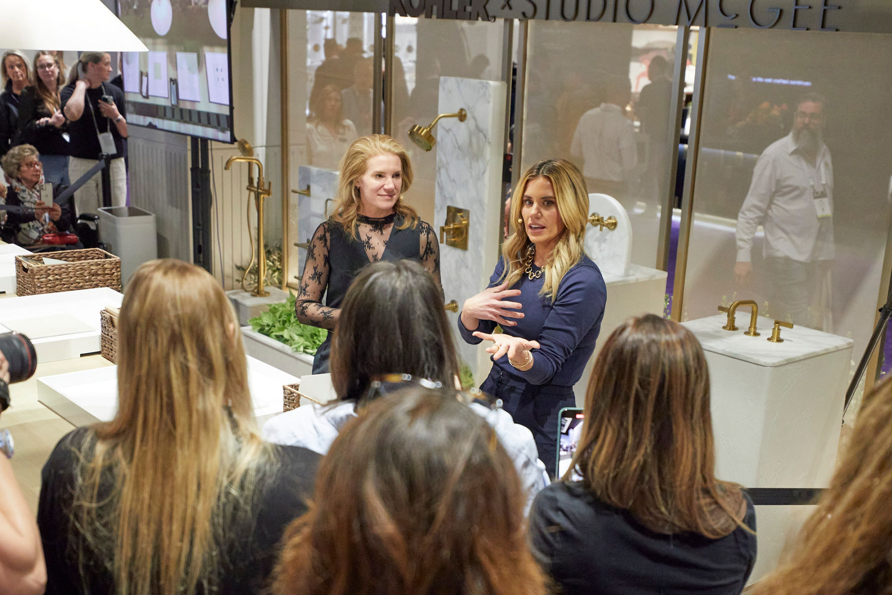  Designer Shea McGee talking to a group of people at the Kitchen and Bath Industry Tradeshow in the Kohler booth