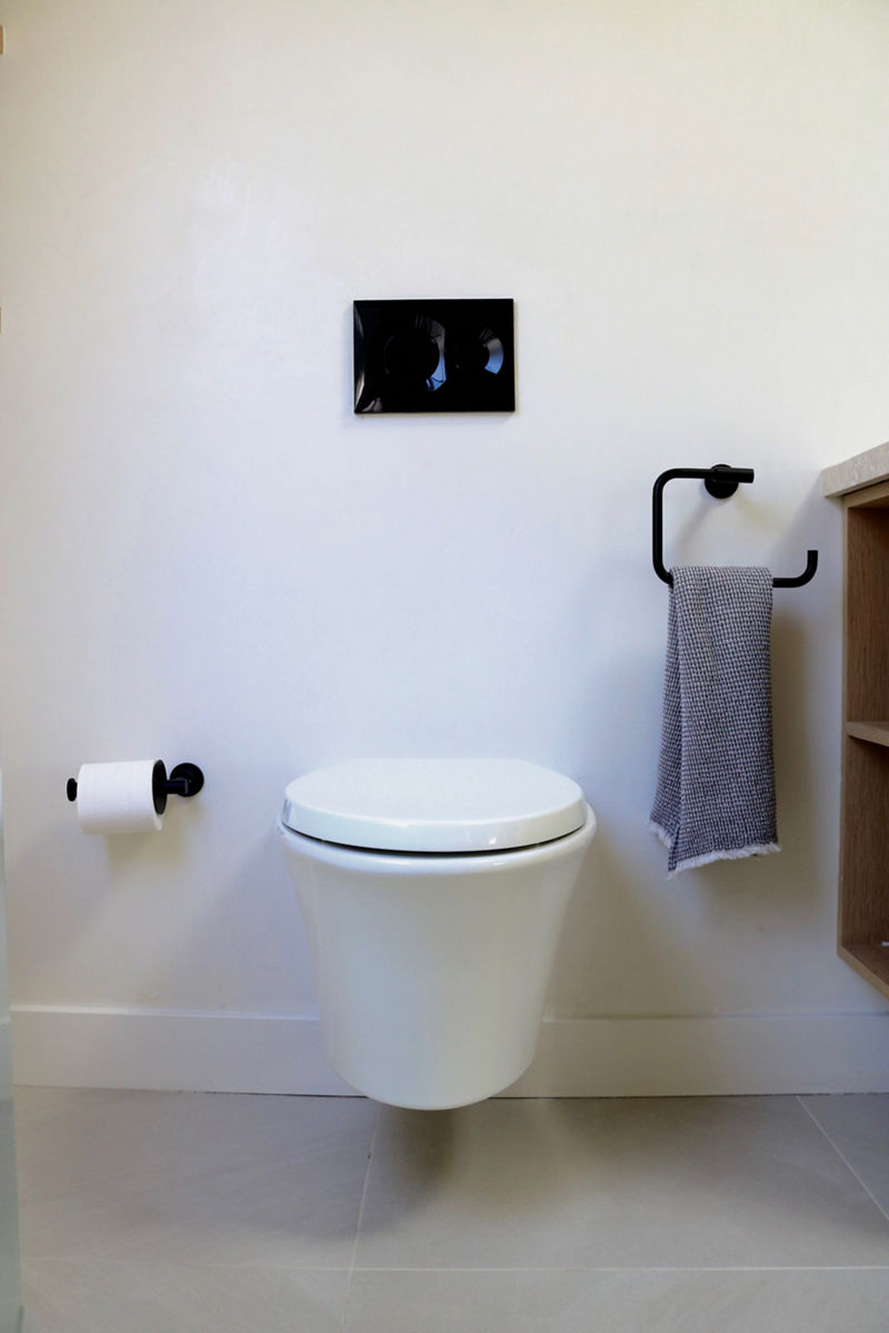A bathroom with gray floors, white walls, and a white KOHLER wall-mounted toilet.