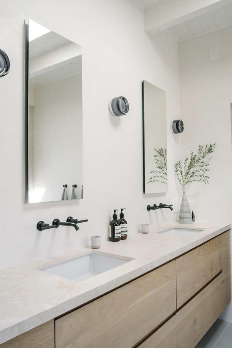 A bathroom with clean, Japandi styling features white walls, KOHLER Matte Black wall mounted widespread faucet, white Ceric freestanding bath, and dark gray towels.