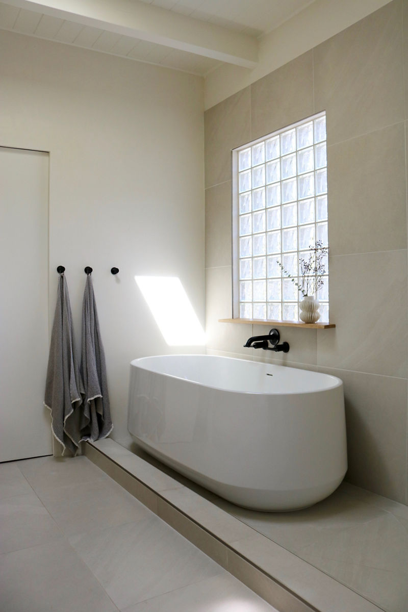 A bathroom with clean, Japandi styling features white walls, KOHLER Matte Black wall mounted widespread faucet, white Ceric freestanding bath, and dark gray towels.