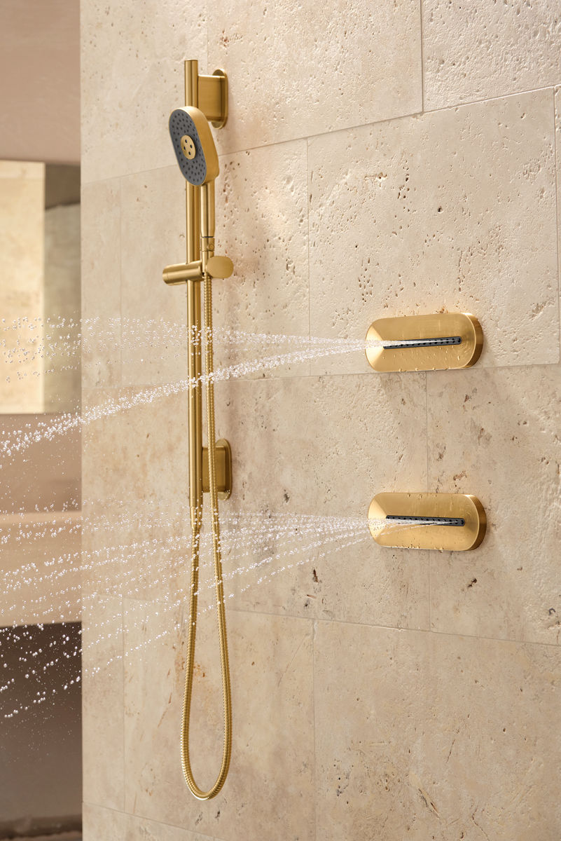 Une douche avec des murs de couleur sable, une douchette KOHLER Statement et des jets corporels ovales.