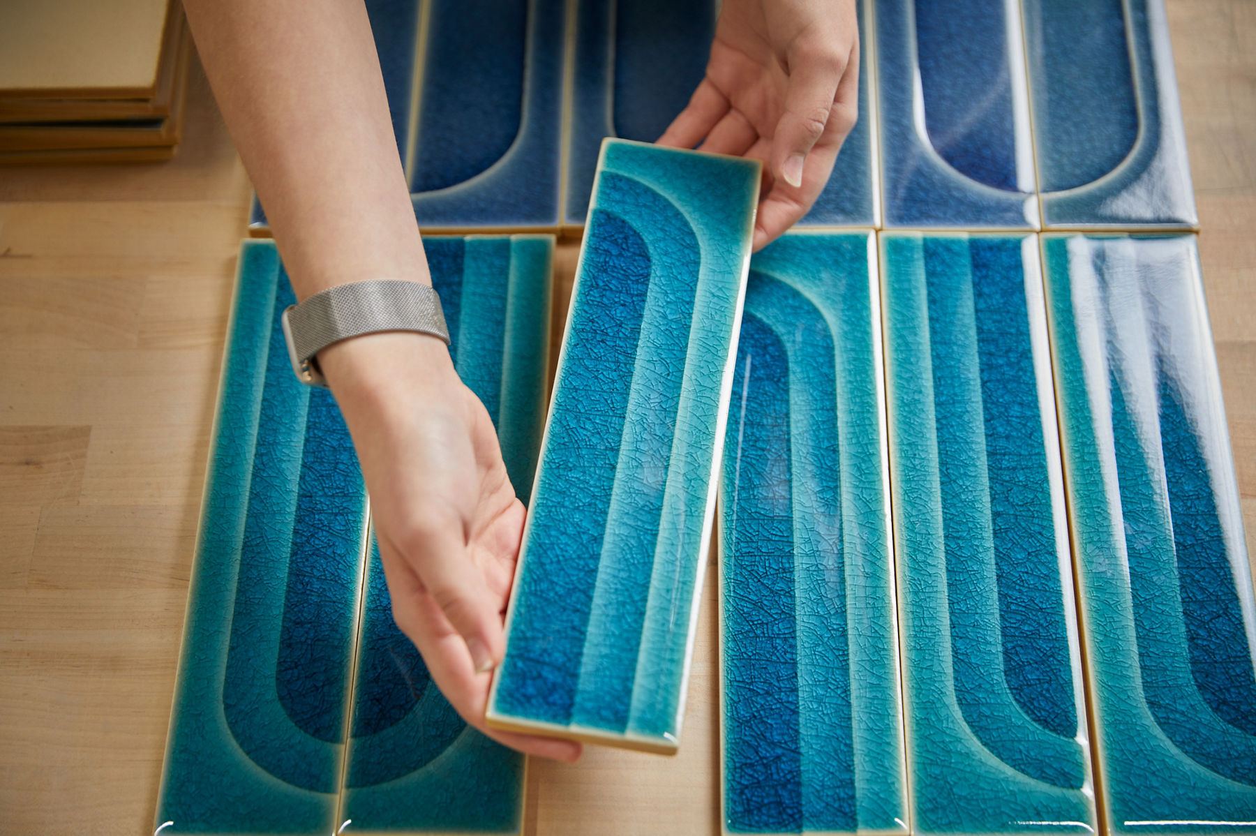 Une personne tenant un carreau bleu créé par le WasteLAB de KOHLER montre les différents dégradés de couleurs et le design craquelé dans un motif d’arche.