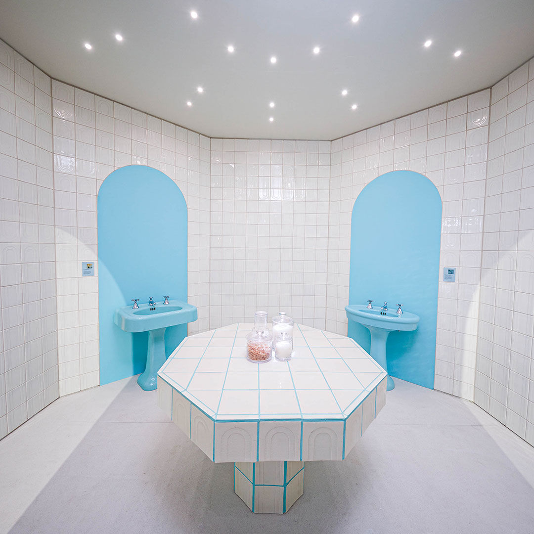 L’intérieur de la pièce chaude à l’installation Naba Debs Design Miami montrant des carreaux au fini os et des lavabos sur colonne de couleur rétro vert printanier.