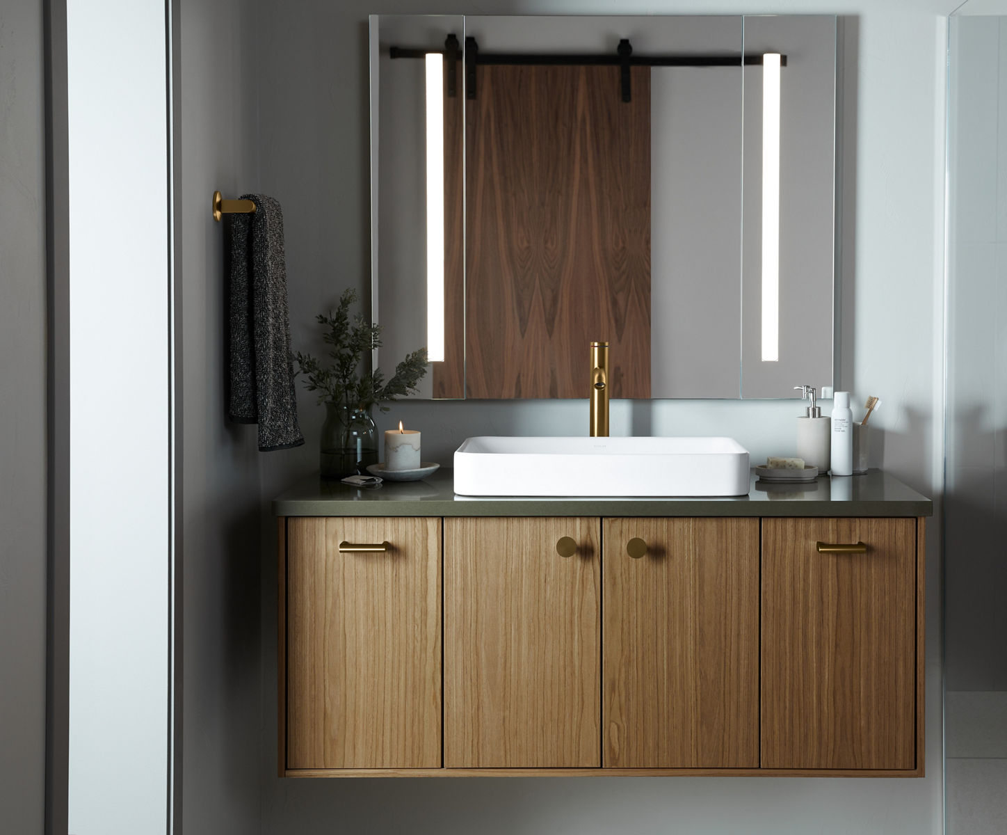 A wood-grain vanity with a green counter top white rectangular vessel sink, brushed brass faucet, and a mirror with integrated lighting on the left and right sides.