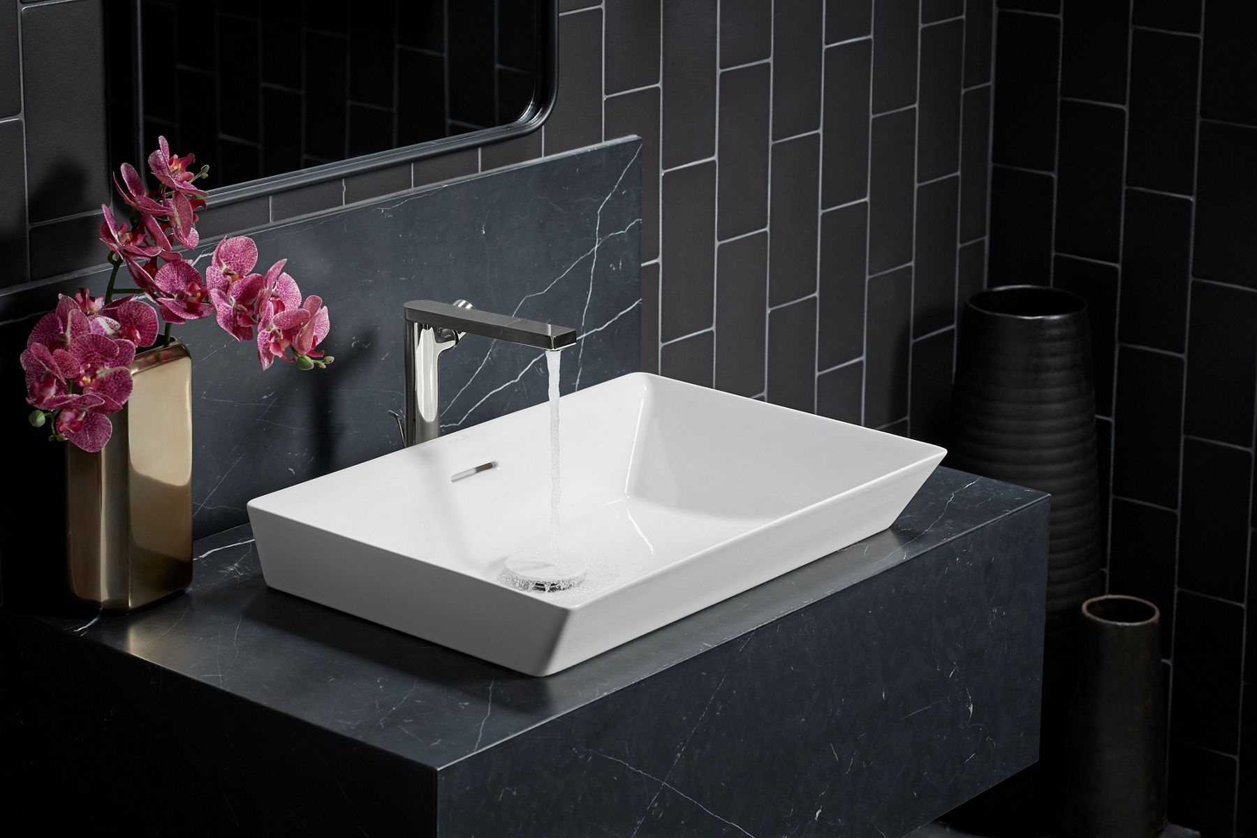 A white Brazn sink on a dark gray quartz vanity with sparse white veining and a dark gray tiled wall.
