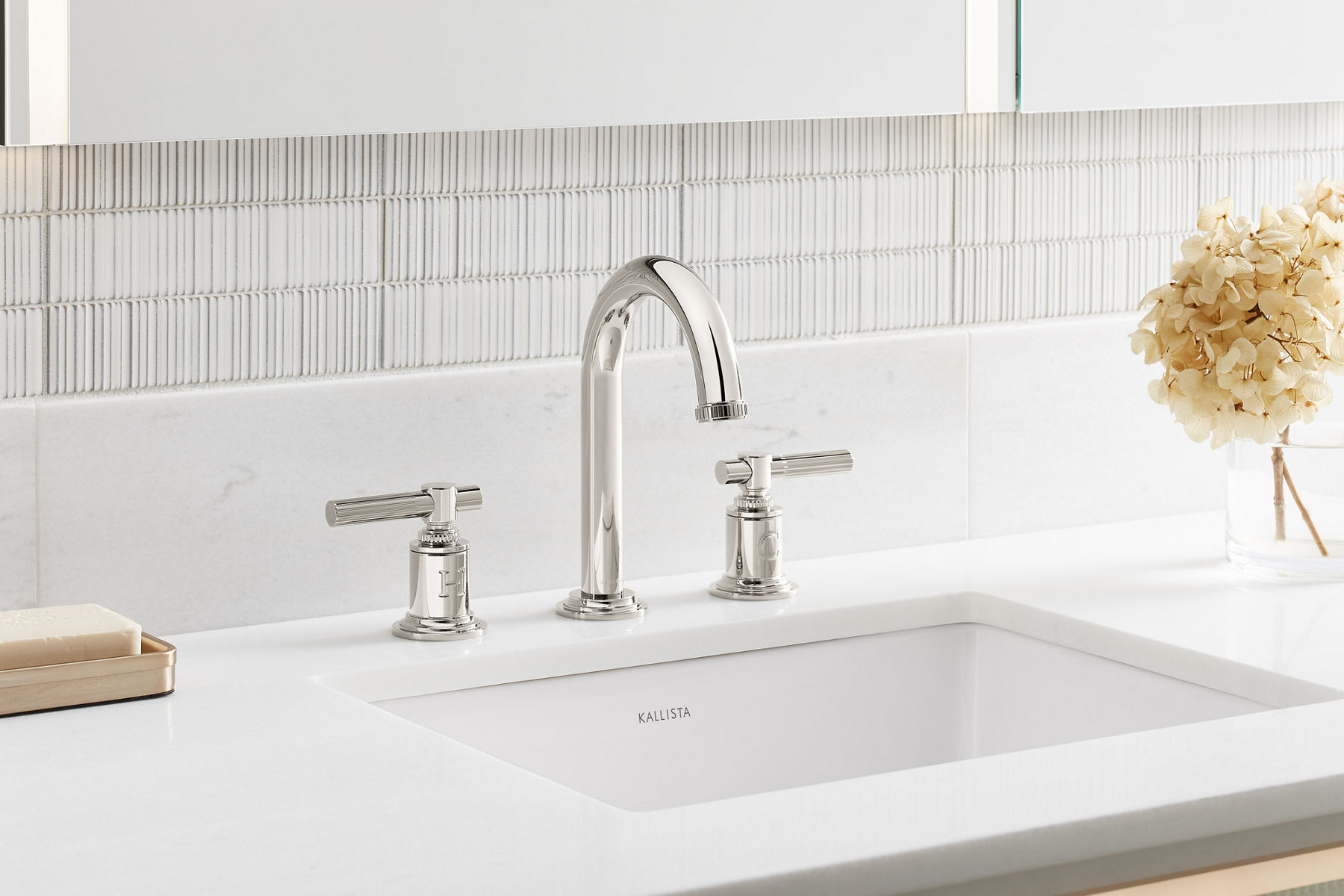 A widespread polished nickel Central Park West faucet on a white counter top with a white undermount sink.