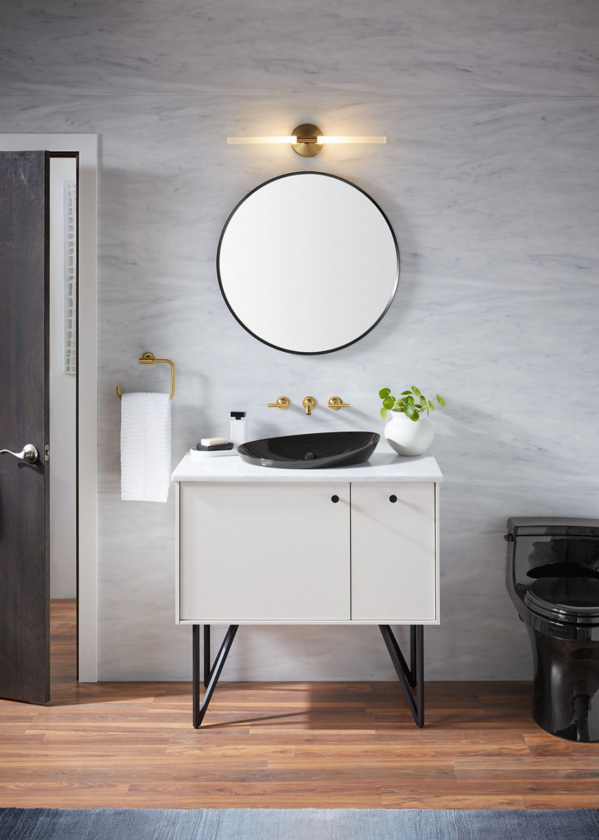 Un miroir rond est suspendu au-dessus d’un meuble-lavabo blanc avec lavabo en surface noir Veil de KOHLER et robinets déployés à installation murale avec poignée à levier.