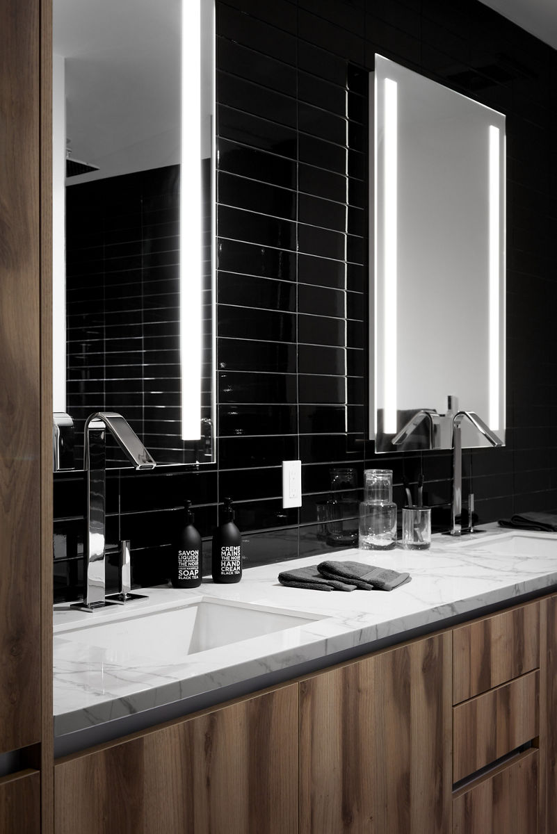Image of contemporary bath with dark tones and black tiling with luminated double vanities and Koher fixtures and fittings.