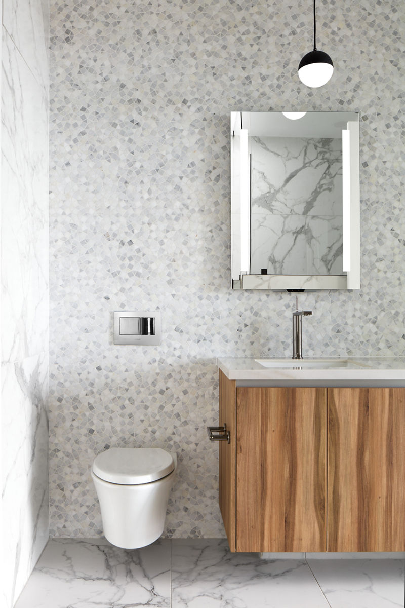 Image modern bathroom with textured walls and marbled flooring with view of wall-mounted intelligent toilet adjacent to bathroom sink and mirror.