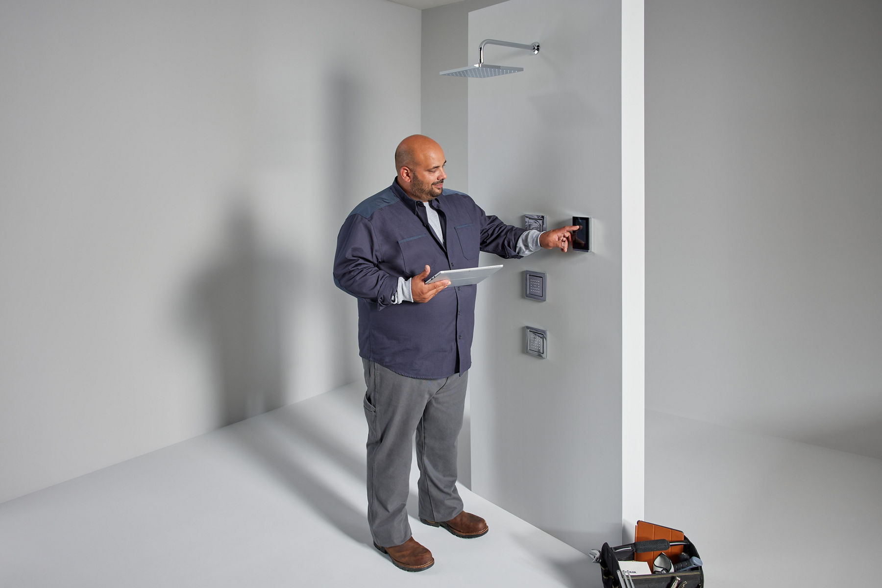 A contractor holding a tablet sets up a wall mount control system for a digital shower.
