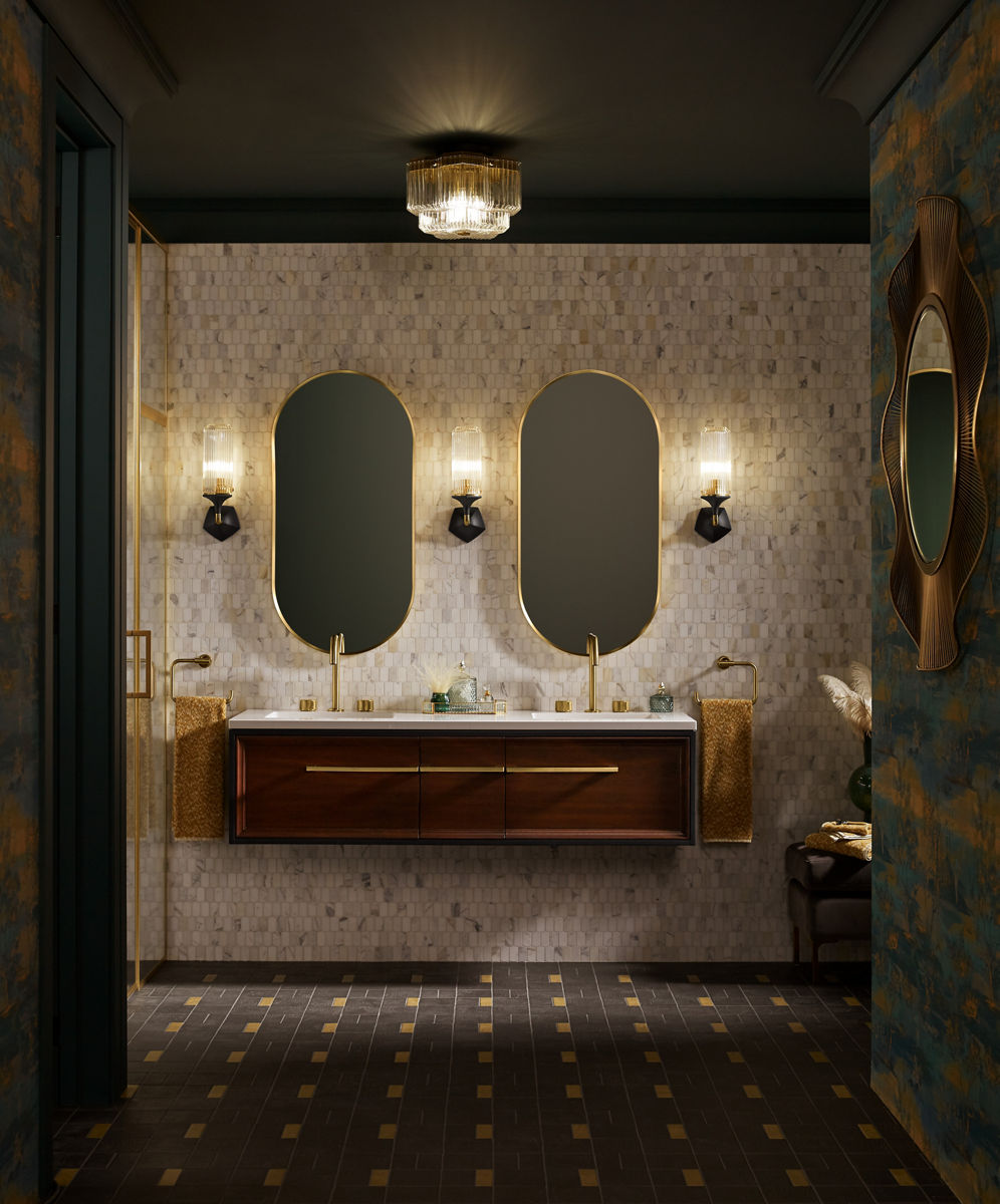 An elegant bathroom with a floating double vanity, gold fixtures, two oval mirrors with gold frames, wall-mounted lights, and a mosaic tile wall.