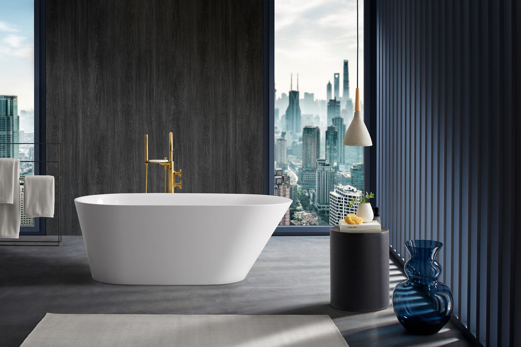 A Brazn freestanding bath in a large open room with a Brushed Brass bath filler and textured gray wall and a window looking out over a city scape.