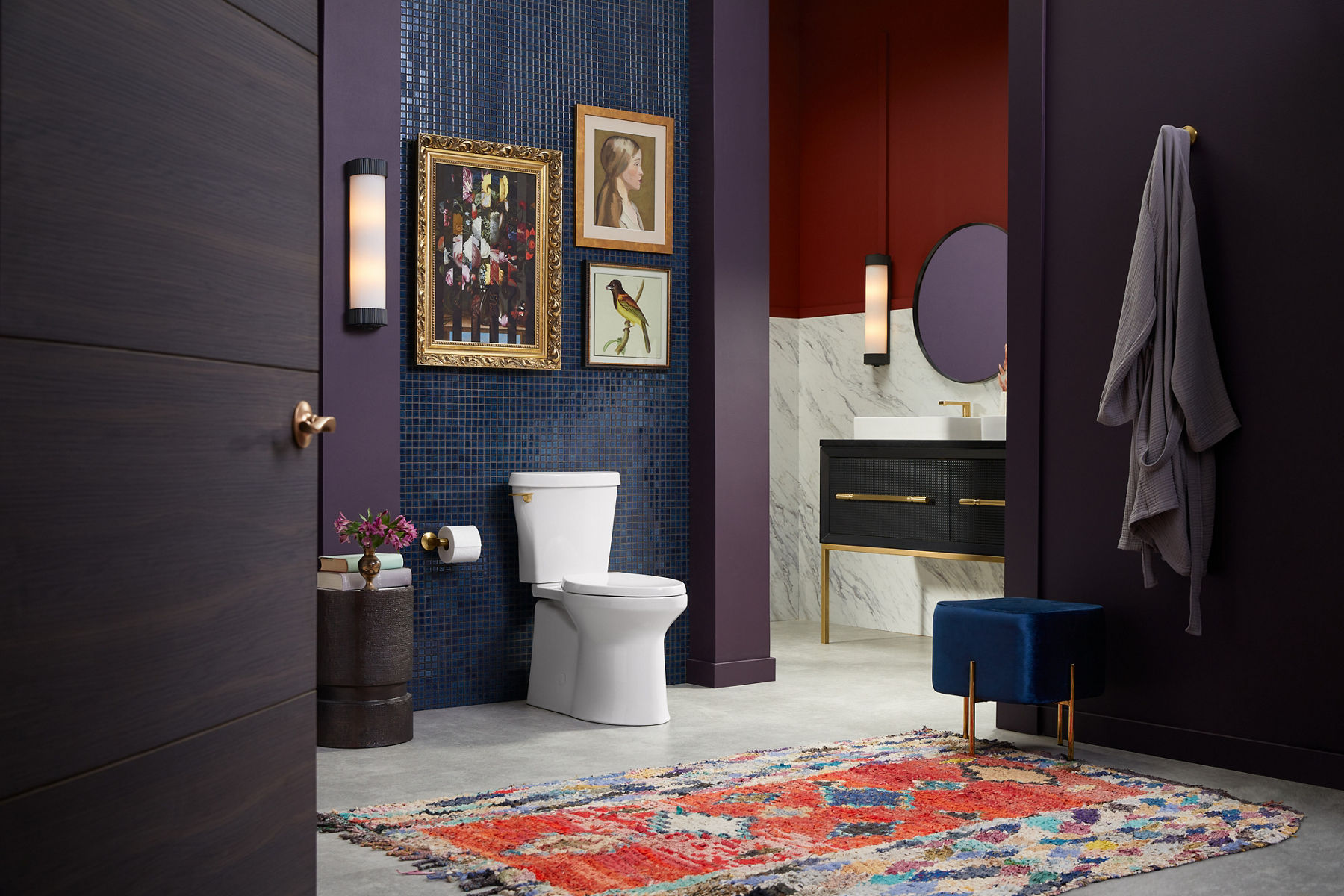 A modern bathroom with a white Kohler toilet and vanity with a round mirror and vessel sink.