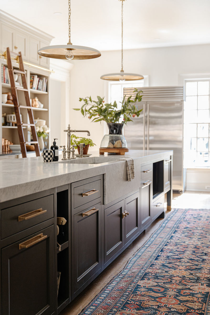A modern farmhouse kitchen with large white-topped island, KOHLER farmhouse sink with Artifacts faucet, two pendants above the island, and open shelving with library ladder.
