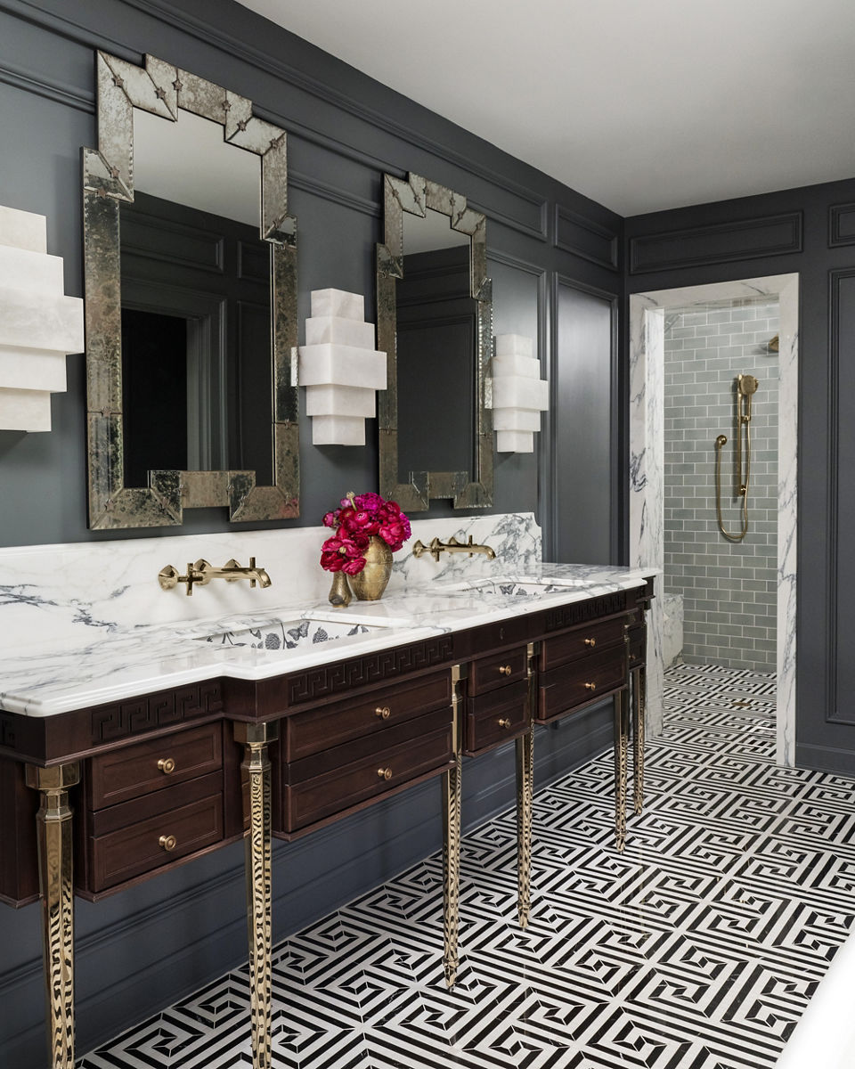 Elegant bathroom with a double vanity featuring a marble countertop, ornate mirrors, and brass fixtures. The design includes dark wood drawers, geometric patterned flooring, and a walk-in shower with brass accents.